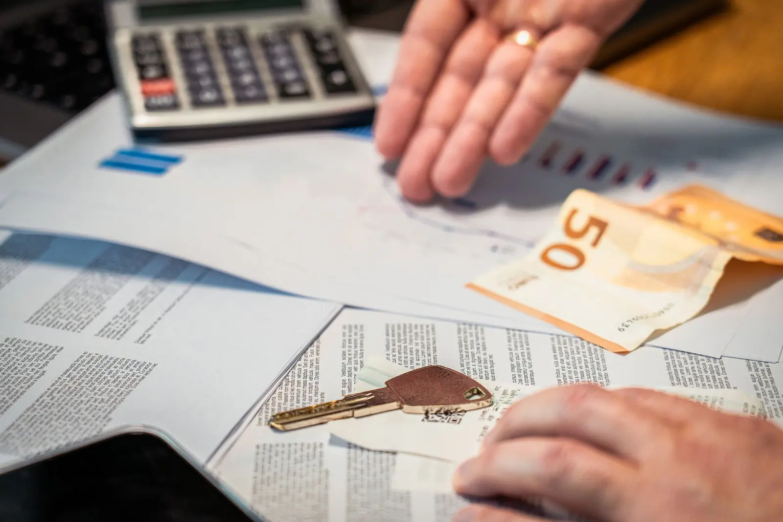 Manos revisando documentación financiera sobre la mesa, con una calculadora, un billete y una llave