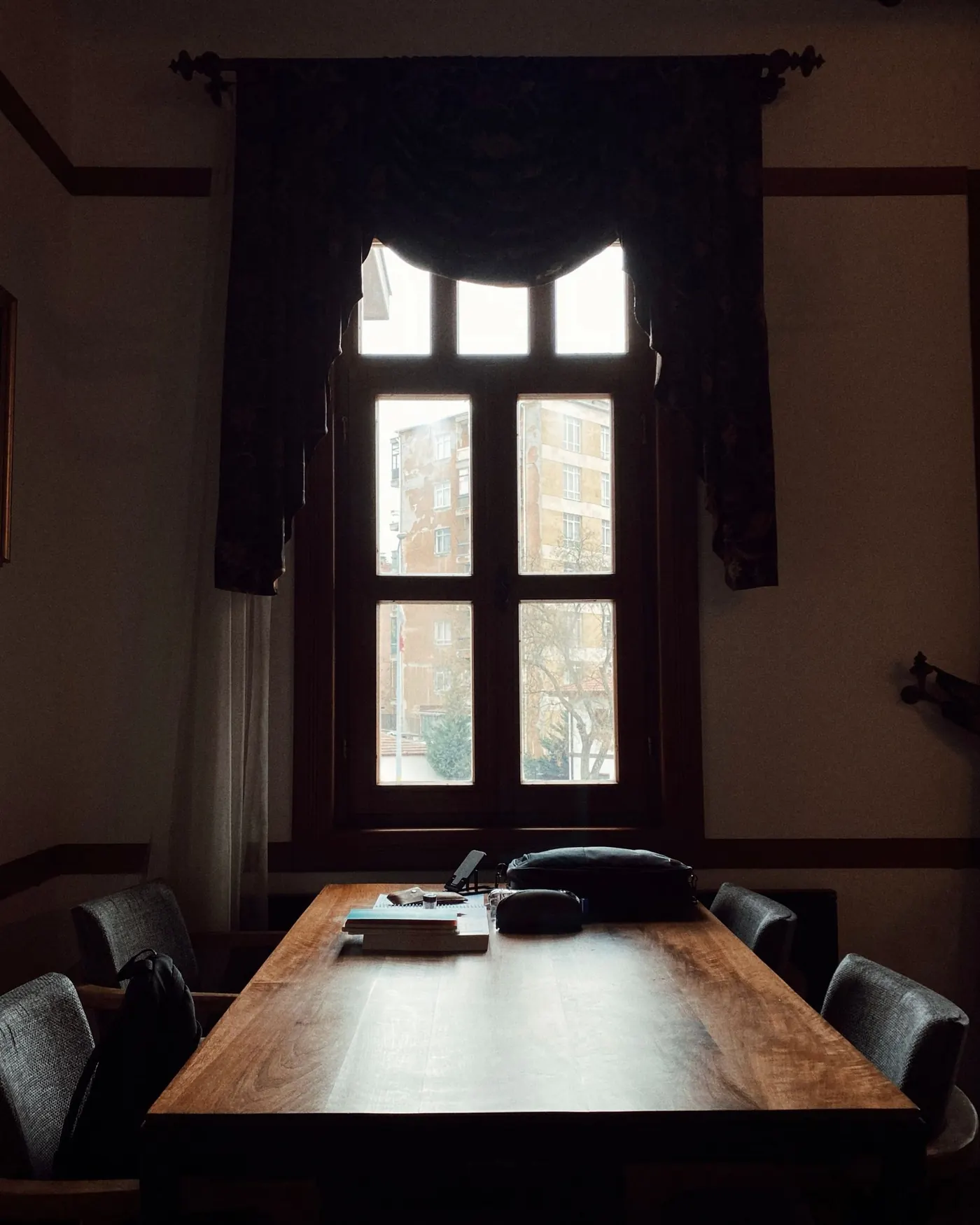 Sala en penumbra con una mesa larga de madera y un ventanal por el que entra la luz de la calle